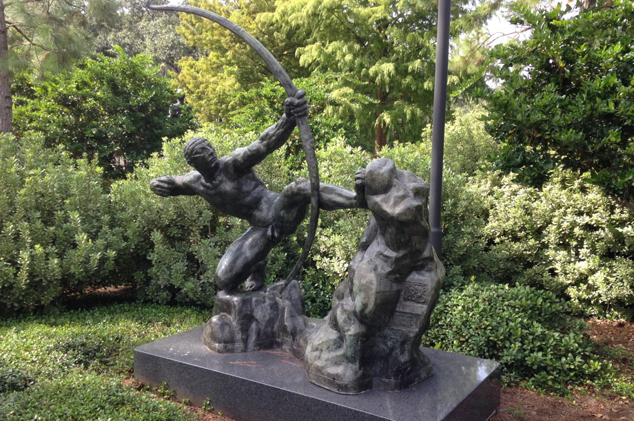 Statue of a muscled figure, crouched, pulling on an enormous bow. Hercules the Archer by Antoine Bourdelle in the New Orleans Museum of Art Sculpture Garden.