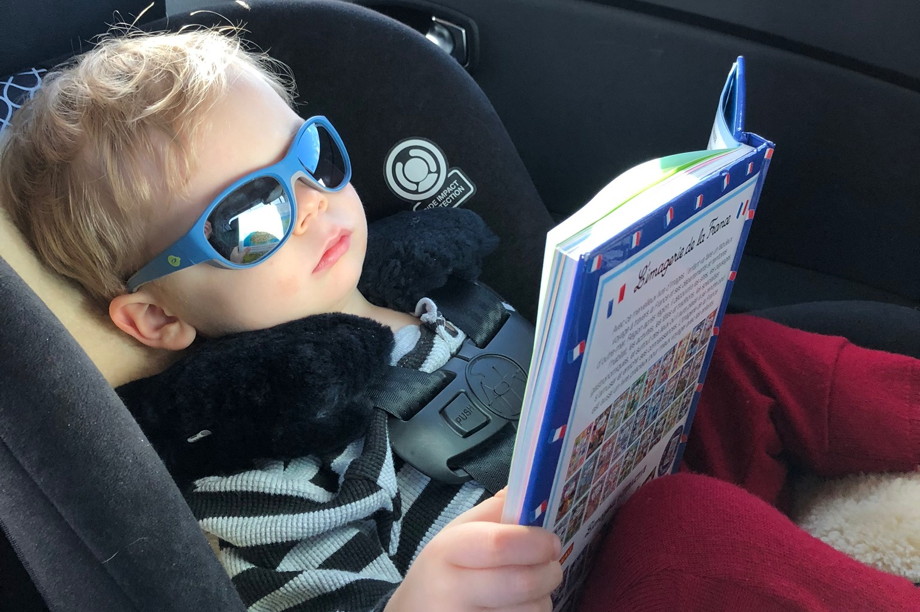 A two year-old in sunglasses reading a French picture book