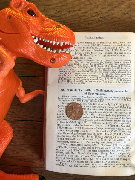 An orange dinosaur inspects a page with small type and a penny on it for scale