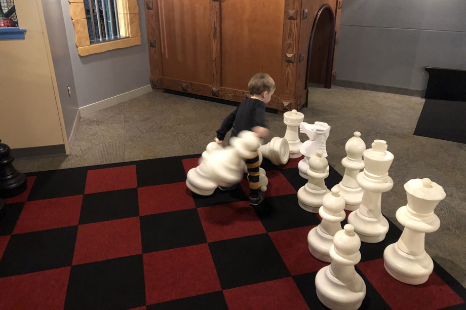 Kid on a child-sized chessboard, knocking over the white pieces