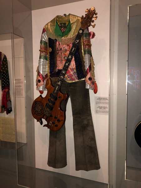 An outrageous shirt in different patterns and fabrics, and a bass guitar, behind plexiglass