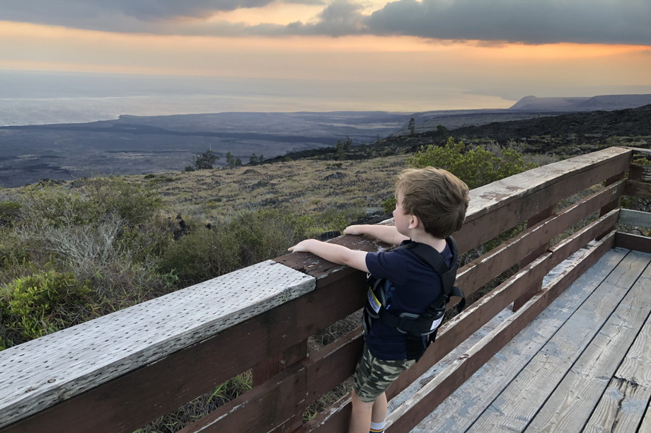A little boy at an overlook point, impressed by the volcanic black shoreline of the Pacific Ocean under a cloudy sky
