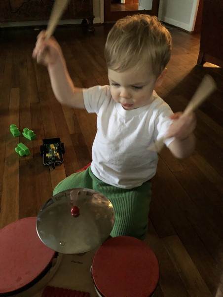 Toddler raising sticks over a toy drum set
