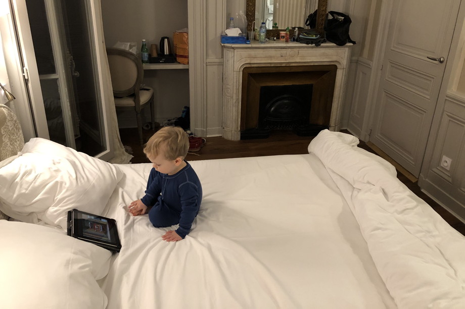 Little boy sitting on a big white bed, looking at a tablet