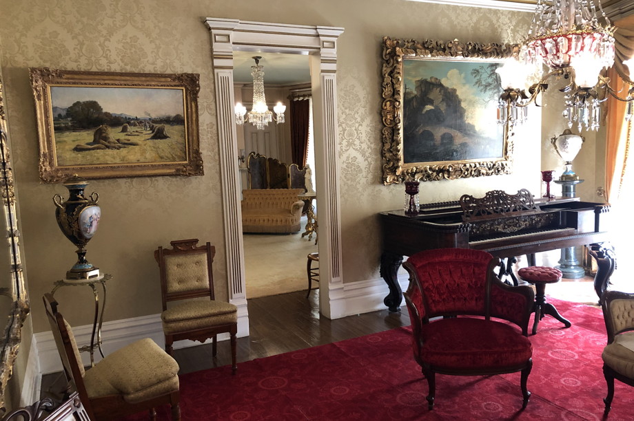 Stately 19th century interior: rugs, chairs, a piano, elaborate lamps