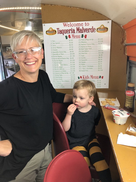 Mom and child sitting on stools eating at a narrow counter with a menu on the wall behind them