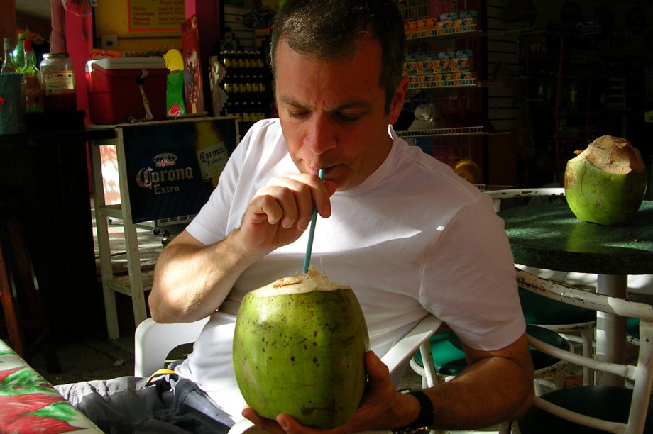 Me in an outdoor restaurant drinking from a green coconut with a long straw