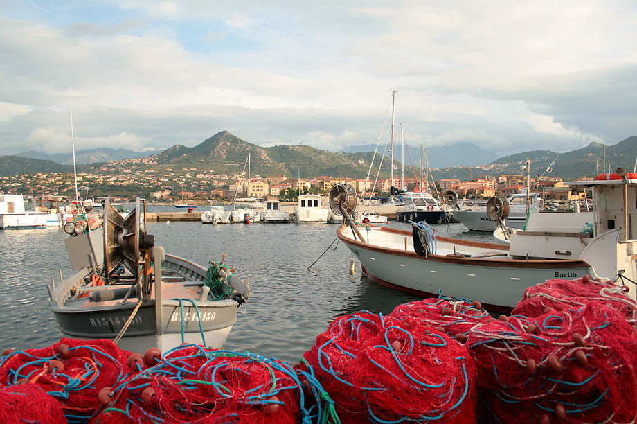 Boats in a harbor with red fishing nets in the foreground and mountains in the background