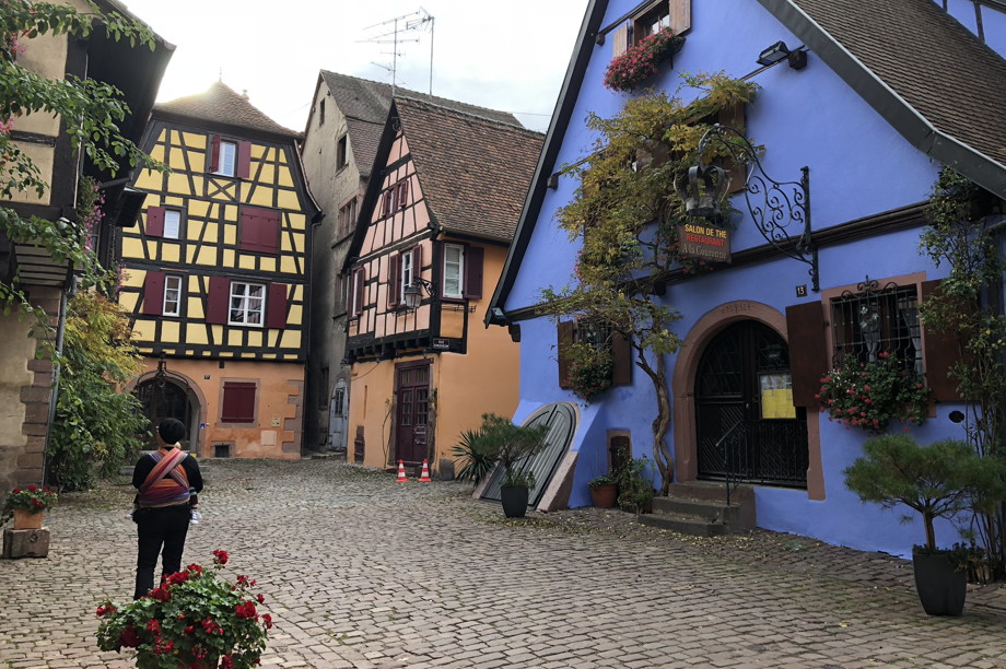 A cobblestone cul-de-sac lined with squat timbered houses painted yellow, salmon, and sky blue in Riquewihr, France