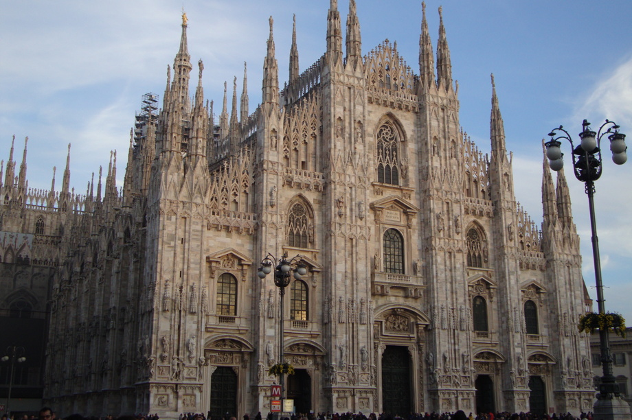 A triangular shaped, light pink marble building with narrow turrets. The Milan Duomo.