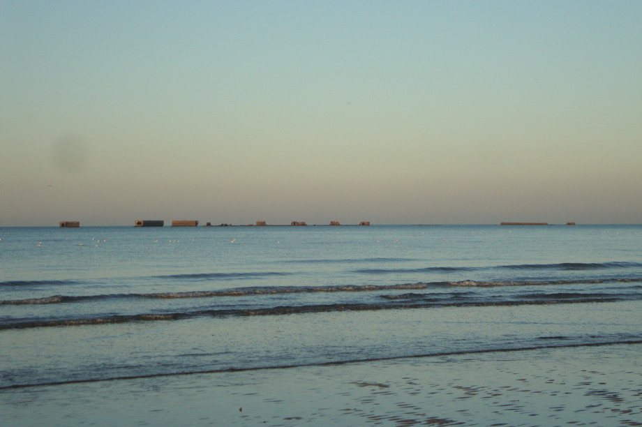 An empty beach at sunset, with large dashes along the horizon that look like elongated train cars