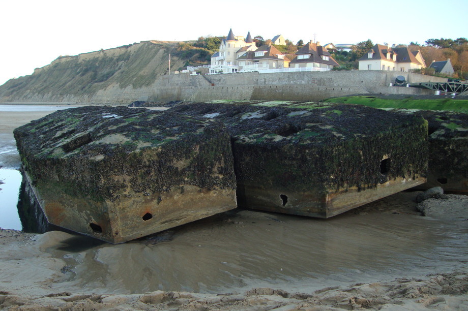 Large concrete blocks, covered in barnacles and moss, sitting on the beach