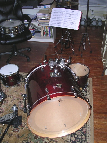 A half-assembled cherry red drum set, with pieces strewn all over the floor