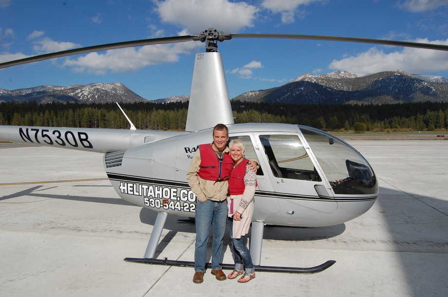 Ferociously attractive couple in front of a helicopter, with mountains in the background