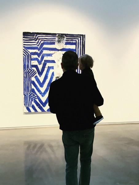 Father and son in silhouette looking at an abstract painting of blue and white lines