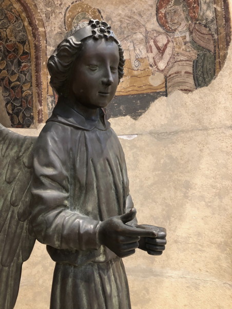 Statue of an angel with a slight smirk, a fresco is in the background