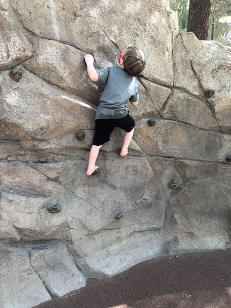 A barefoot kid climbing a wall, looking pretty confident