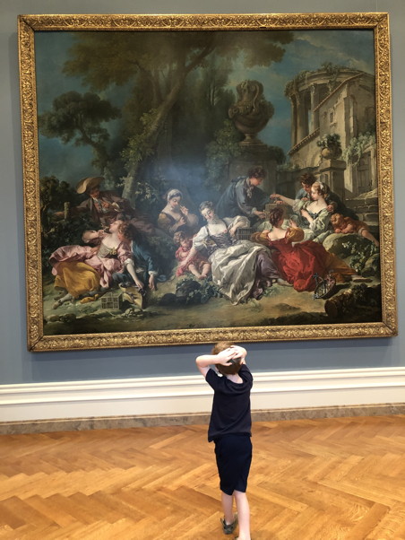 A child with his hands on his head, looking at an almost 300 year-old painting of a lazy, semi-romantic picnic
