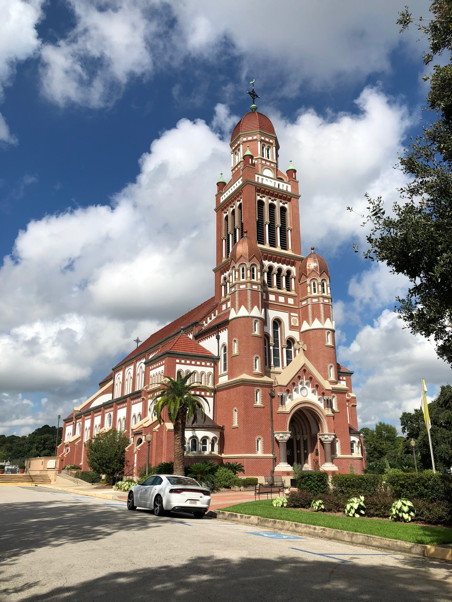 Large tower of a red brick church ascending toward a blue sky with puffy clouds