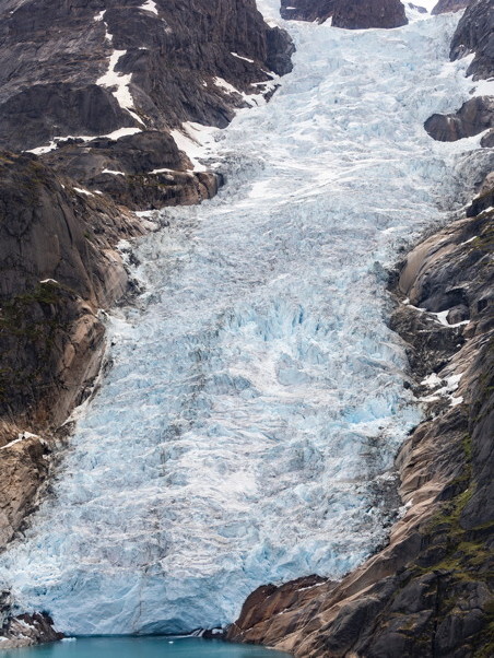 Bluish snow and ice running down to the water, with jagged rock on either side