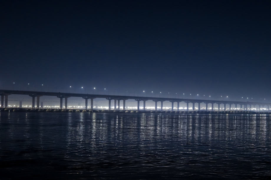 A bridge at night, illuminated by the city on the shore